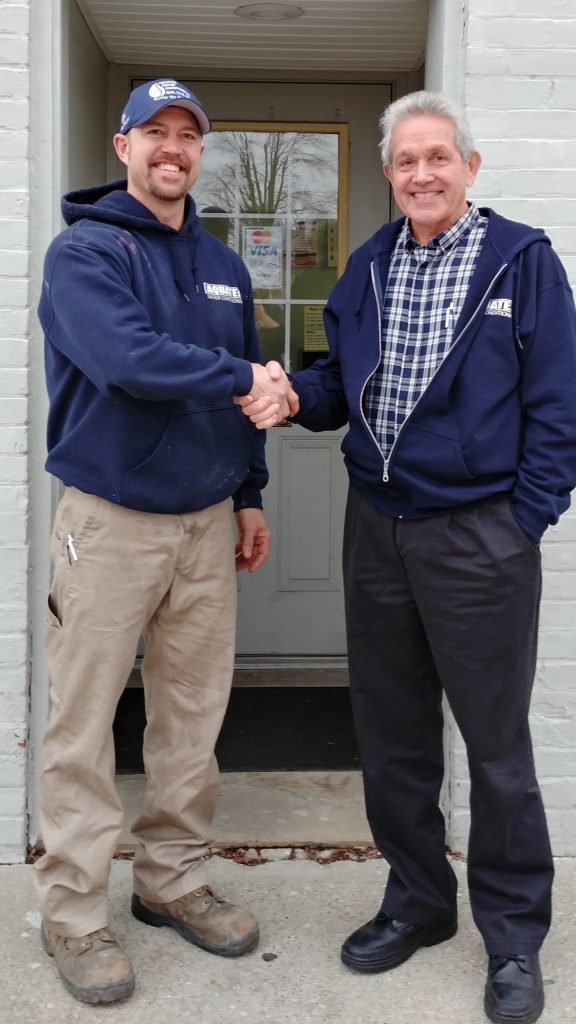 Brandon Schindler, current owner, and Bill Fortier, former owner shake hands in front of Aquatek Water Conditioning.